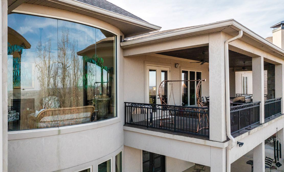 A custom home's curved windows and balcony overlooking trees